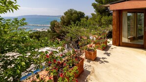 Una propiedad costera con terraza, plantas en macetas y vistas al mar y montañas lejanas.