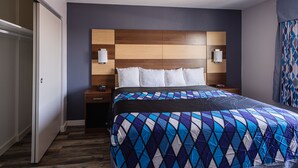 A hotel room with a large bed, a wooden headboard, two bedside tables with lamps, and a sliding door.