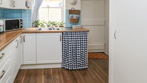 Una cocina con armarios blancos, encimera de madera, un fregadero, un microondas y una ventana con cortinas azules.