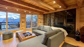 Uma sala de estar moderna com um sofá seccional, uma mesa de centro de madeira e vista para uma montanha através de grandes portas de vidro deslizantes.
