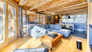 Interior de cabana rústica moderna com um amplo sofá seccional em formato de L, uma mesa de centro de madeira e uma cozinha com mesa e cadeiras.