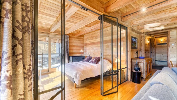 Interior de uma cabana de madeira com uma cama, um sofá e um painel de vidro.