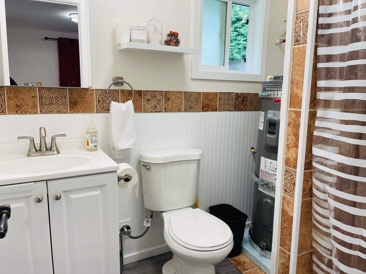 Um banheiro com pia, vaso sanitário e chuveiro brancos. Há uma toalha pendurada na parede e uma prateleira acima do vaso.