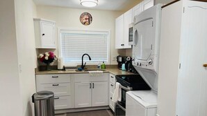 Una cocina compacta con alacenas blancas, un lavamanos, una estufa y un microondas.