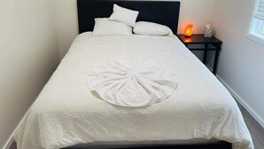Una cama bien hecha con una colcha blanca y un adorno central de toalla blanca.
