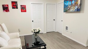 Una sala de estar con un sofá blanco, una mesa de centro negra con un jarrón de flores blancas, y tres cuadros en la pared.
