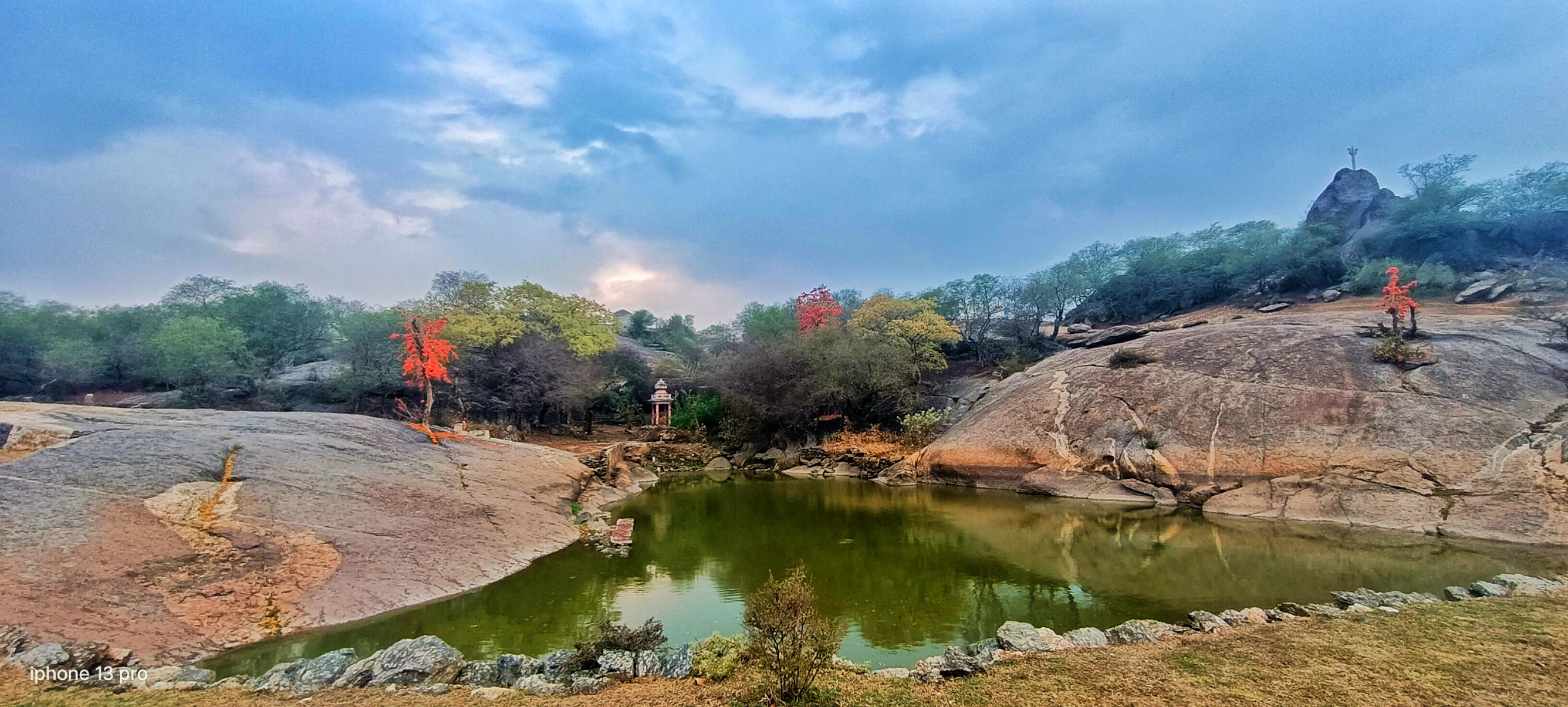 A serene landscape with a pond, rocky terrain, and trees.