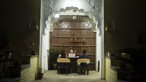 A traditional entrance with a wooden door and decorative arches, leading to a seating area with wicker chairs and a table. - Barabagh Deogarh (Devgarh)