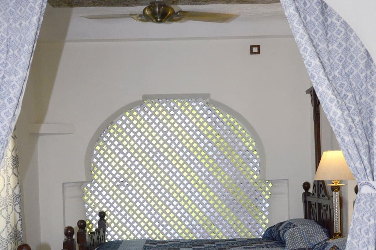 Quarto com cama, janela com cortina estampada e luminária.