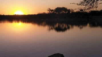 A sunset over a calm lake with a silhouette of a person on a rock.