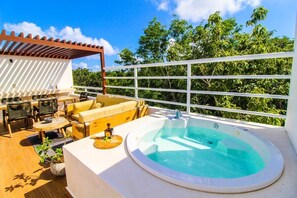 Une terrasse sur le toit dotée d’un jacuzzi, d’un espace salon extérieur et offrant une vue sur une végétation luxuriante.