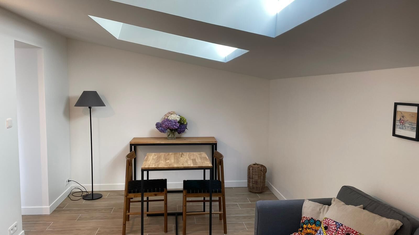 A room with a skylight, a table with chairs, a lamp, a sofa, and a framed picture on the wall.
