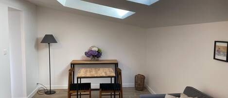 A room with a skylight, a table with chairs, a lamp, a sofa, and a framed picture on the wall.