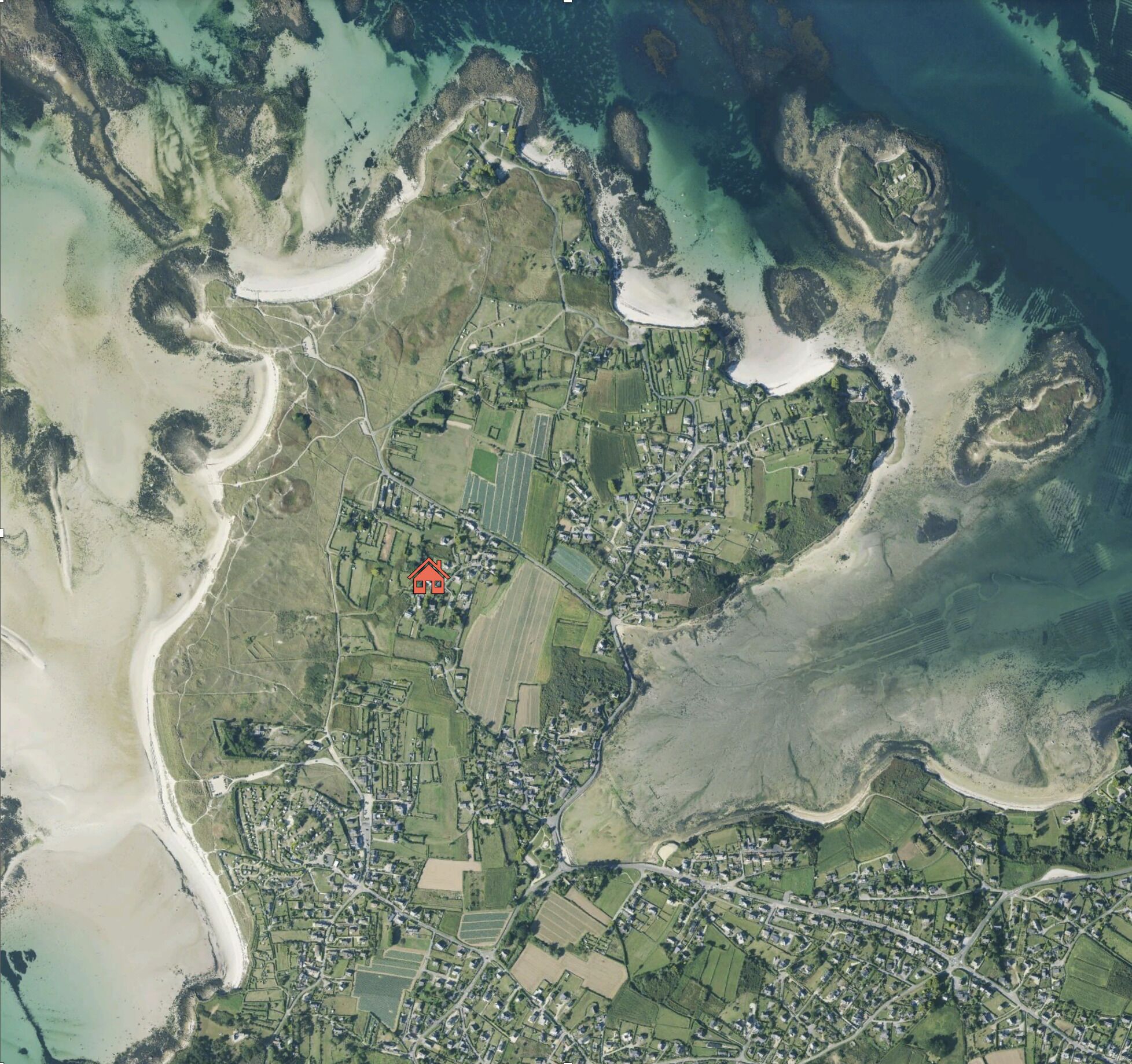 An aerial view of a coastal town with a central cluster of buildings, surrounded by fields and a beach.