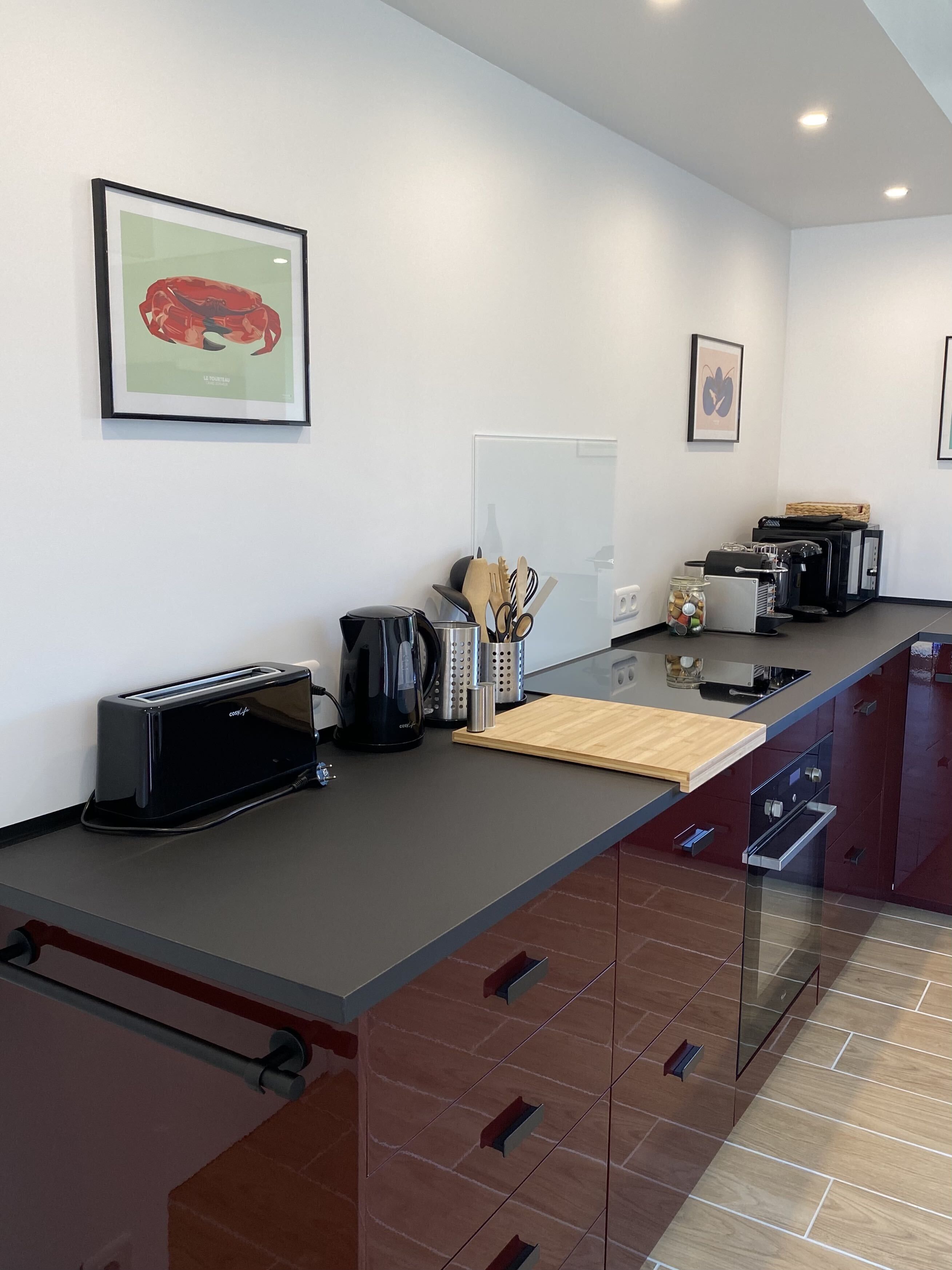 A modern kitchen with a toaster, coffee maker, and a wooden cutting board on the counter.