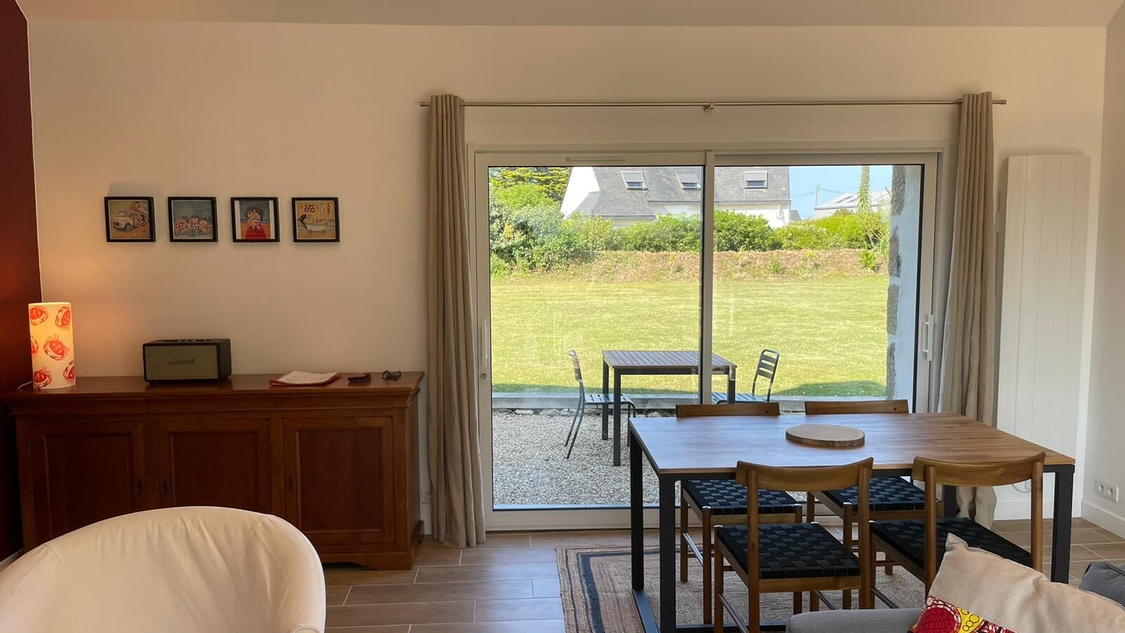 Une pièce comprenant un coin repas, un meuble avec une lampe, et donnant sur un jardin grâce à une porte coulissante.