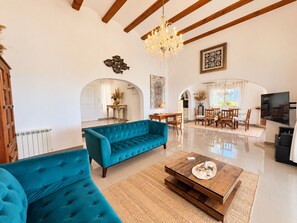 A spacious living room with a blue sofa, wooden dining table, and a chandelier. - Villa with panoramic views all inclusive La Sella DJ (Pedreguer)