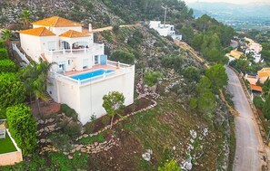 Una villa bianca con piscina blu, immersa nel verde e con una strada tortuosa.