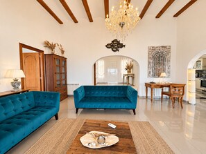 A spacious living room with a blue sofa, a wooden cabinet, and a chandelier. - Villa La Sella DJ with Private Pool and Golf Views (Pedreguer)