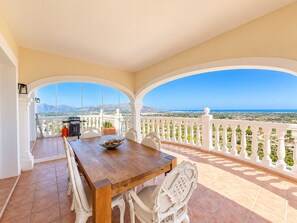 Un balcón con mesa de madera y sillas blancas, con vistas a un paisaje pintoresco.