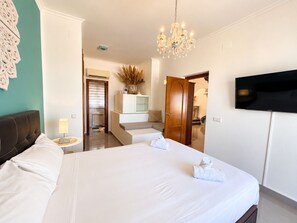 Una habitación de hotel con una cama grande, un televisor montado en la pared y una araña.