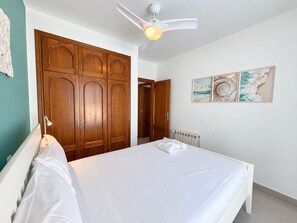 A bedroom with a bed, a ceiling fan, wooden wardrobe, and artwork on the wall.