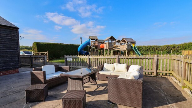Un patio al aire libre con mobiliario de mimbre y una zona de juegos al fondo.