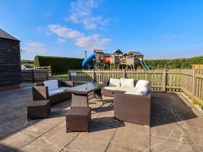An outdoor patio with wicker furniture and a play area in the background. - The Old Nursery (Malpas)