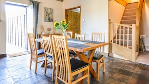 Un comedor con una mesa y sillas de madera, un jarrón con girasoles y una escalera que sube a un nivel superior.