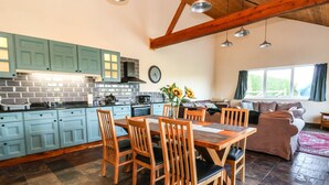Una cocina amplia con armarios verde azulado, un comedor con sillas de madera y una sala de estar con sofá marrón.