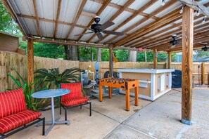 A covered outdoor patio with a foosball table, red striped sofas, and a small round table.