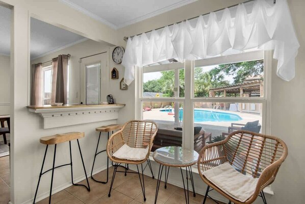 A room with a pool view, wicker chairs, a small table, and a bar area.