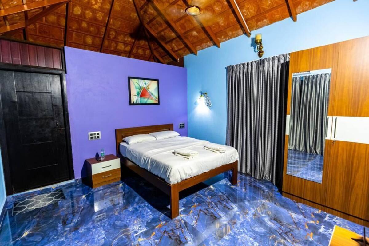 Een slaapkamer met een houten plafond, een bed met wit beddengoed, een paarse muur en een blauwe marmeren vloer.