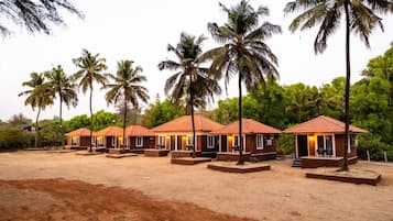 A row of bungalow-style accommodations with tiled roofs, surrounded by palm trees and greenery.