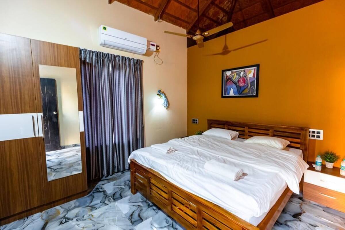 Een slaapkamer met een houten bed, een plafondventilator, een airconditioningapparaat, een spiegel en een schilderij aan de muur.