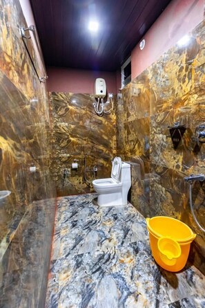 Un baño con tocador de mármol, inodoro, ducha y un cubo amarillo.