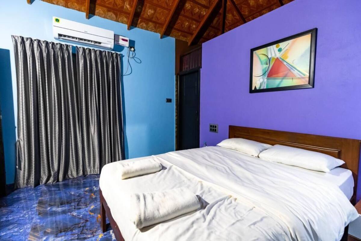 Een hotelkamer met een bed, gordijnen, een airconditioner en een schilderij aan de muur.