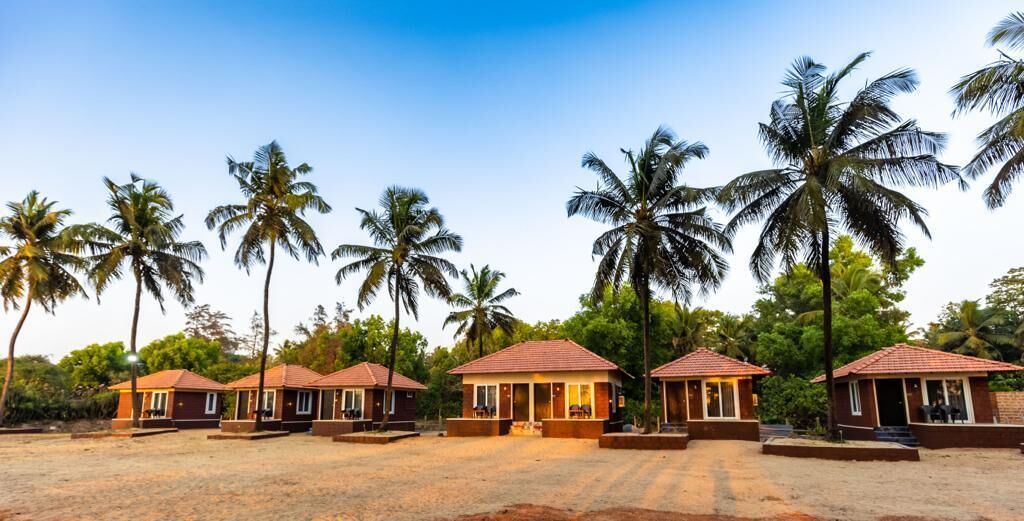 A row of small, single-story buildings with red roofs, surrounded by palm trees.