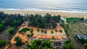 Luchtbeeld van een kustbezit met een strand, palmbomen en meerdere gebouwen met rode daken.