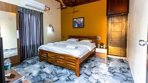 Hotelkamer met een houten bed, marmeren vloer, een airconditioning, een plafondventilator, een schilderij aan de muur en een houten deur.