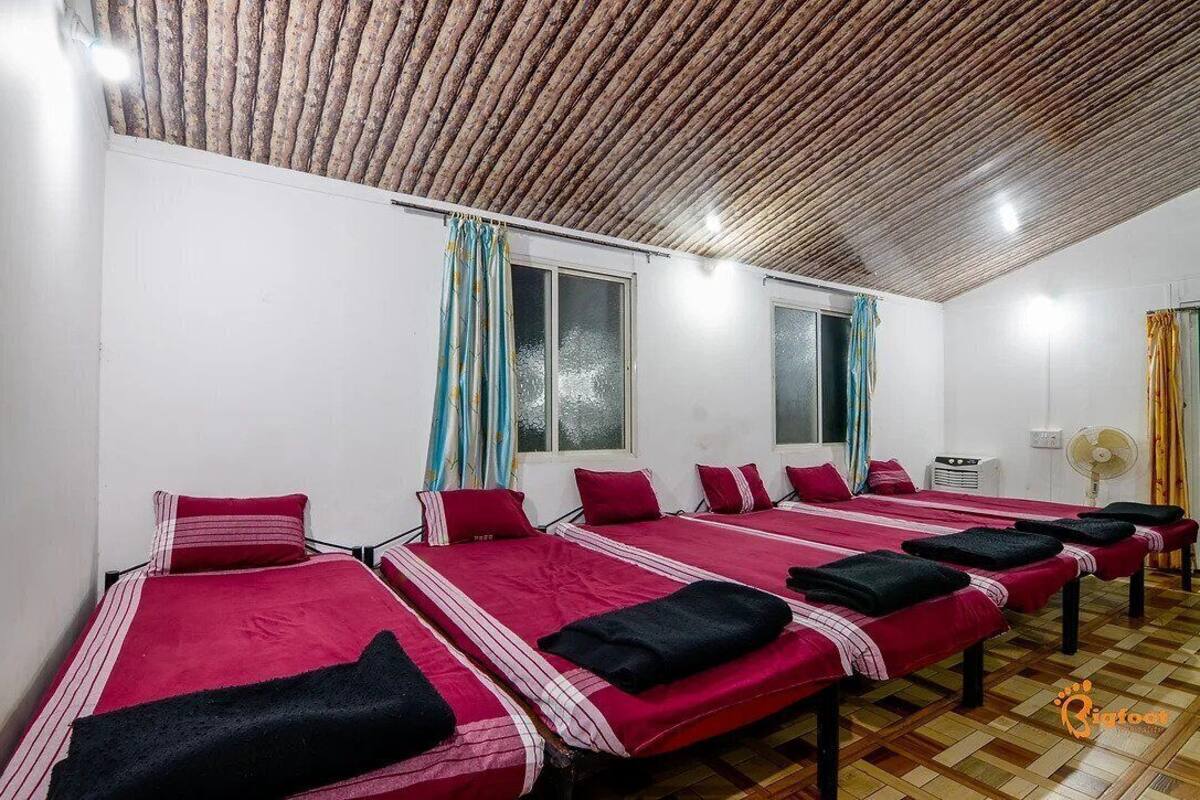A room with six beds arranged in two rows, each with a red bedspread and black towels.
