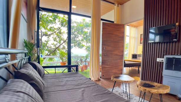 A modern bedroom with a large bed, a wooden ceiling, and a view of greenery outside. - Mango Forest Agro Tourism Resort (Pune)