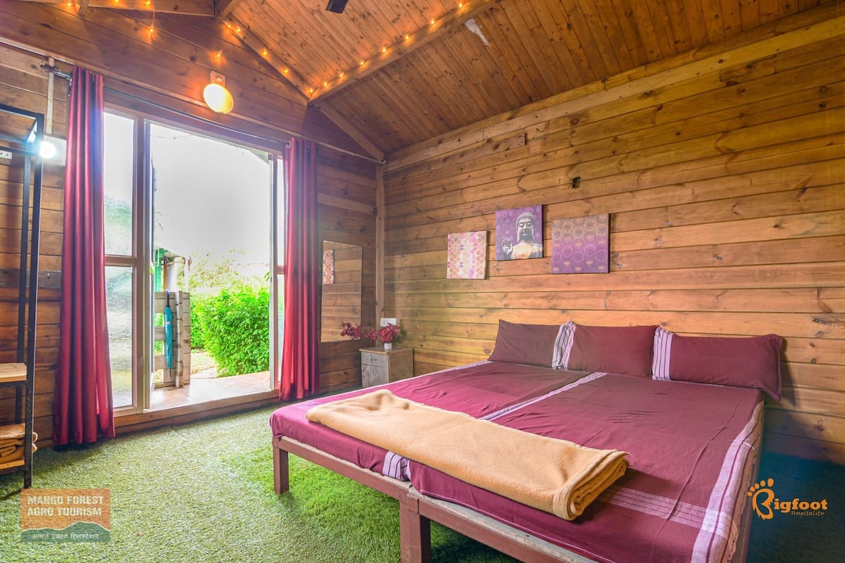 A wooden cabin room with a bed, a bench, and a sliding glass door leading to a garden.