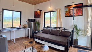 A modern room with a bed, a desk, and a large window offering a view of the outdoors. - Mango Forest Agro Tourism Resort (Pune)