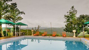 A pool with lounge chairs and a view of mountains. - Mango Forest Agro Tourism Resort (Pune)