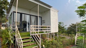 A modern house with a covered porch, a staircase with artificial grass, and a garden with various plants. - Mango Forest Agro Tourism Resort (Pune)