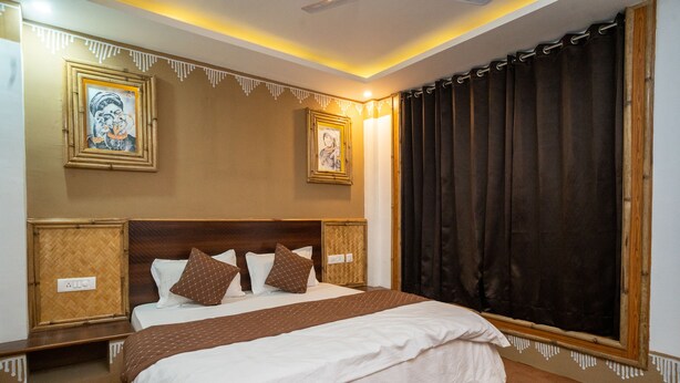 A neatly made bed with a brown headboard and white bedding, a large window with dark curtains, and two framed pictures on the wall. - Mussoorie (Dehradun)