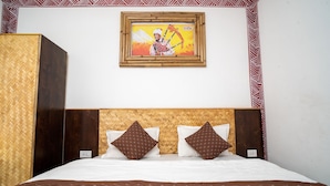 A hotel room with a bed, two pillows, a wooden headboard, a framed picture on the wall, and a patterned border on the wall. - Mussoorie (Dehradun)