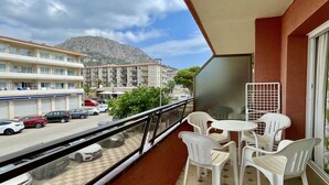 A balcony with white plastic chairs and a table, overlooking a street with parked cars and buildings, and a mountain in the background. - SALLES BEACH 2 (Estartit)
