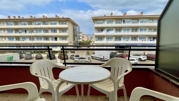A balcony with two white plastic chairs and a small round table, overlooking a street with parked cars and buildings. - SALLES BEACH 2 (Estartit)